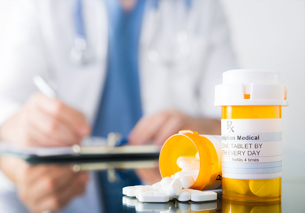 Two pill bottles containing large white tablets sit in the foreground; in the background a doctor writes a prescription